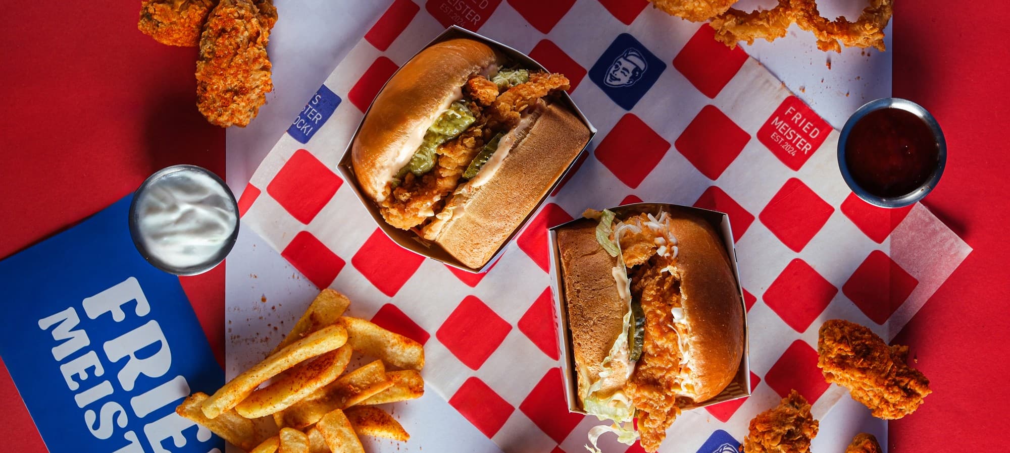 Kareli kâğıt üstünde iki çıtır tavuk burger, patates, tenders ve soslar